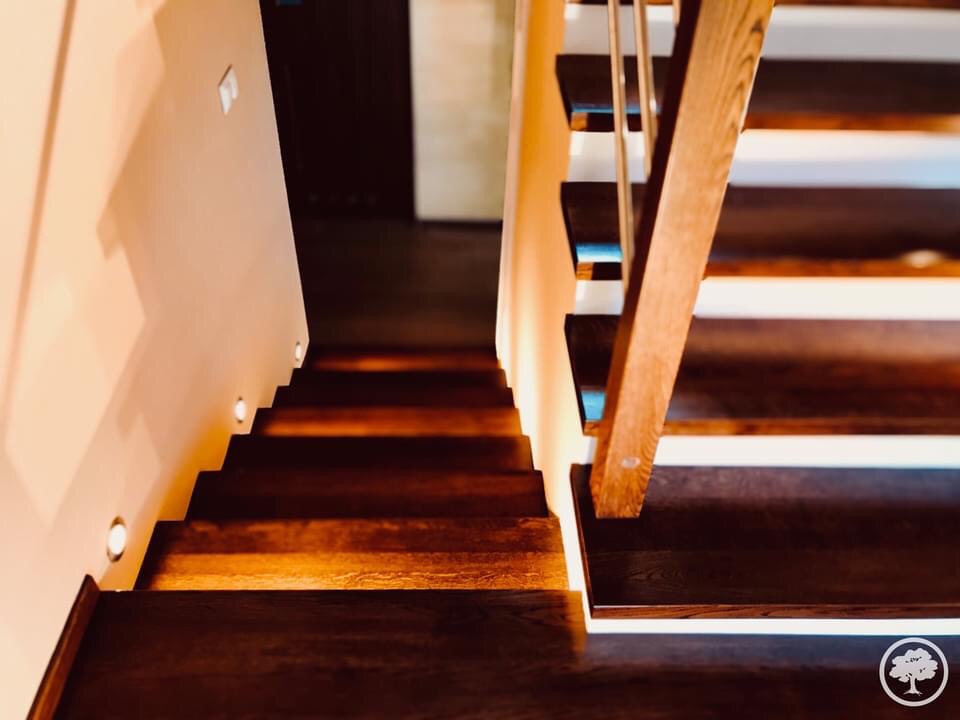 Nowoczesne schody z ciemnego drewna z podświetleniem LED wzdłuż ściany i białymi podstopnicami, widok z dołu.