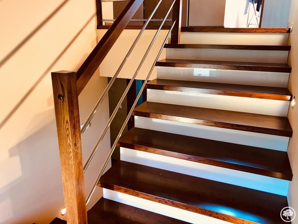 Nowoczesne schody z ciemnego drewna z podświetleniem LED pod stopniami i metalową balustradą, widok z dołu.