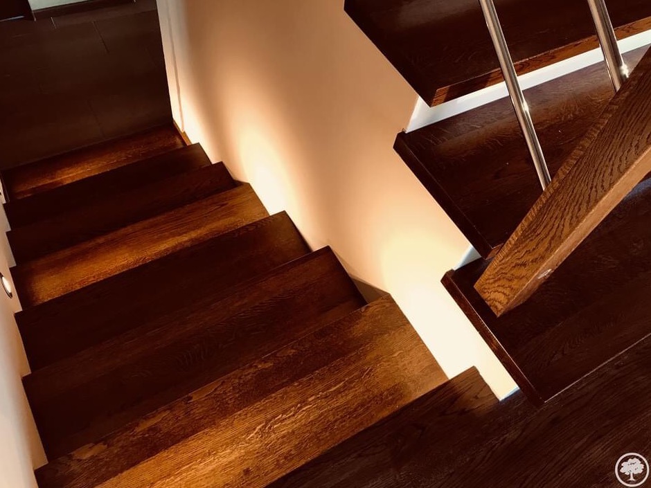 Ciemne, drewniane schody z metalową balustradą, widok z góry, oświetlone ciepłym światłem, z widoczną strukturą drewna i minimalistycznym wykończeniem.