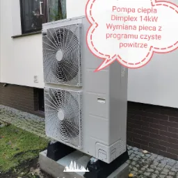 Zewnętrzna jednostka pompy ciepła Dimplex 14kW, zamontowana na betonowym fundamencie z czarnymi podkładkami antywibracyjnymi, z widocznym oknem w tle i informacją o wymianie pieca w ramach programu...