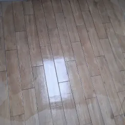 Ułożona, błyszcząca podłoga z płytek imitujących drewno, ułożonych w regularny wzór, z widocznymi fugami i odbiciem światła.