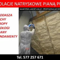 Pracownik w kombinezonie ochronnym natryskuje pianę izolacyjną na poddaszu, widoczne drewniane elementy konstrukcyjne dachu i gruba warstwa nałożonej piany.