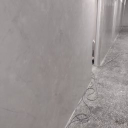 GAC-BUD Usługi Budowlane - Ściana z szarą, dekoracyjną fakturą w korytarzu, widoczne przewody na podłodze.