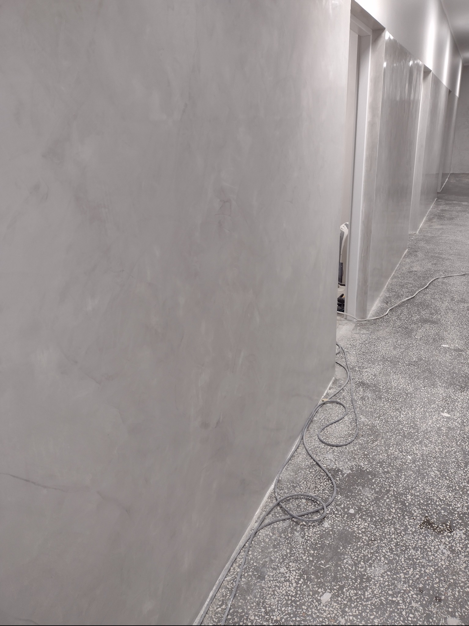 Ściana z szarą, dekoracyjną fakturą w korytarzu, widoczne przewody na podłodze.