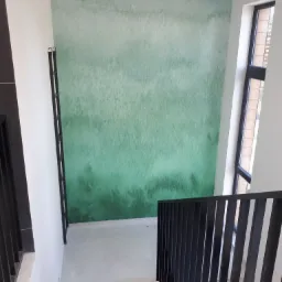 Ściana w klatce schodowej z gradientem zieleni, widok z góry schodów, czarna balustrada, okno po prawej stronie.