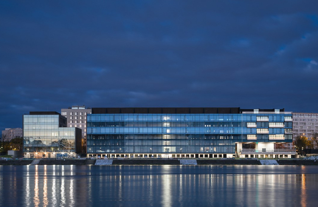 Nowoczesny budynek biurowy z licznymi oknami, oświetlony w nocy, odbijający się w tafli wody.
