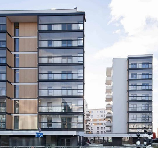 Nowoczesne budynki mieszkalne z przeszklonymi balkonami, widok z zewnątrz w słoneczny dzień.