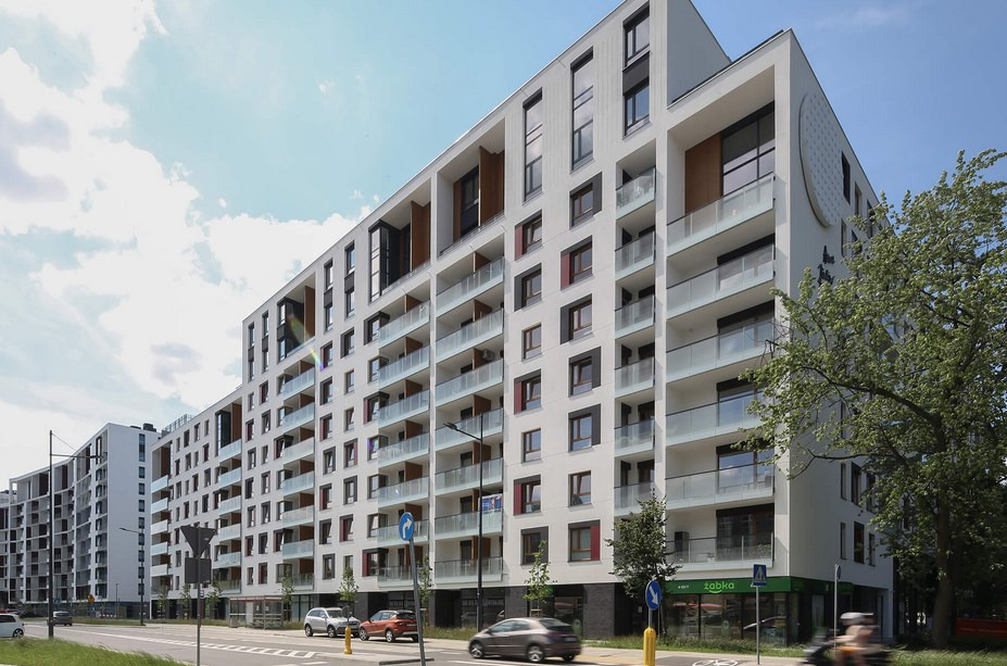 Nowoczesny budynek mieszkalny z balkonami i sklepem Żabka na parterze, widok z perspektywy ulicy w słoneczny dzień.