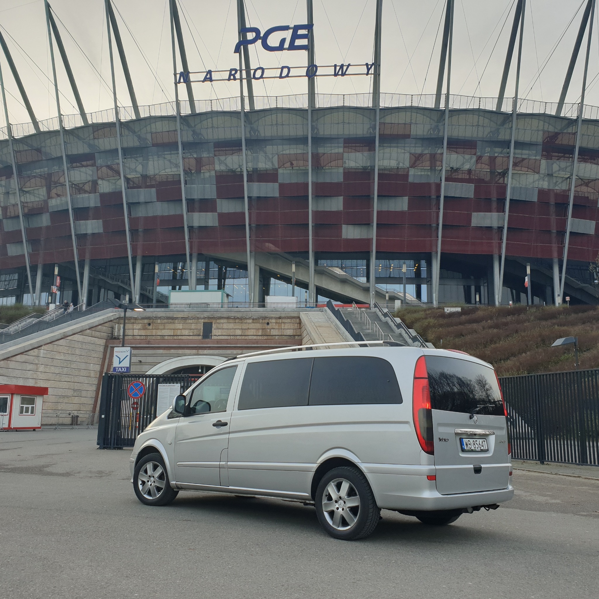 Srebrny van Mercedes Vito zaparkowany na tle Stadionu Narodowego w Warszawie, widok z tyłu.