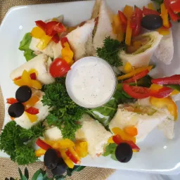 Elegancko podane kanapki na białym talerzu z dipem, udekorowane kolorowymi paprykami, pomidorami i oliwkami, realizacja z Radomia.