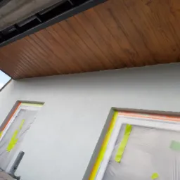 Ocieplona elewacja budynku z drewnianą podbitką dachową i zabezpieczonymi oknami folią malarską.