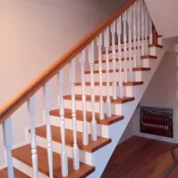 Klasyczne schody z drewnianymi stopniami i białymi balustradami, widoczne z boku, z podestem i panelem sterowania pod nimi.