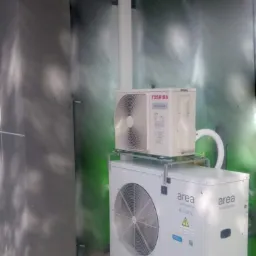 Dwie jednostki zewnętrzne klimatyzacji zamontowane jedna na drugiej na zewnątrz budynku, z widocznymi przewodami i elementami montażowymi, na tle ściany z efektem graffiti.