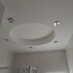 Wykończona łazienka z podwieszanym sufitem z okrągłym wgłębieniem i oświetleniem punktowym, widoczna kabina prysznicowa i podświetlane lustro.