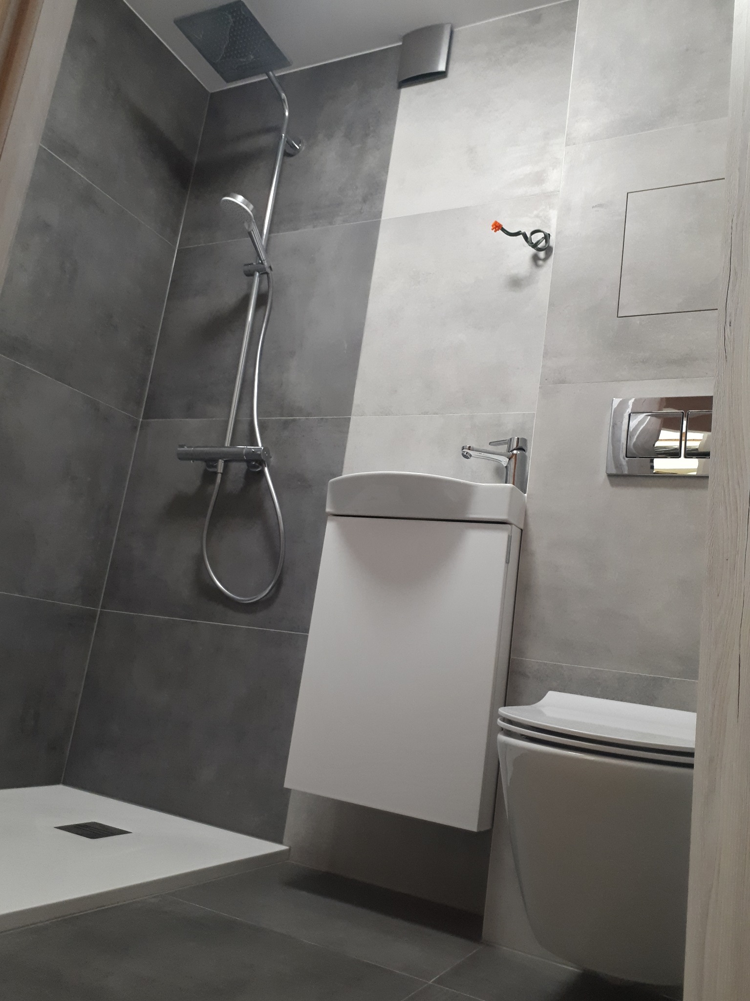 Nowoczesna łazienka z szarymi płytkami, kabiną prysznicową typu walk-in, umywalką nablatową z szafką i podwieszaną toaletą.