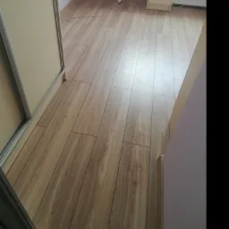 Ułożone panele podłogowe w pokoju z szafą przesuwną i szafką nocną, widoczne łączenia paneli.