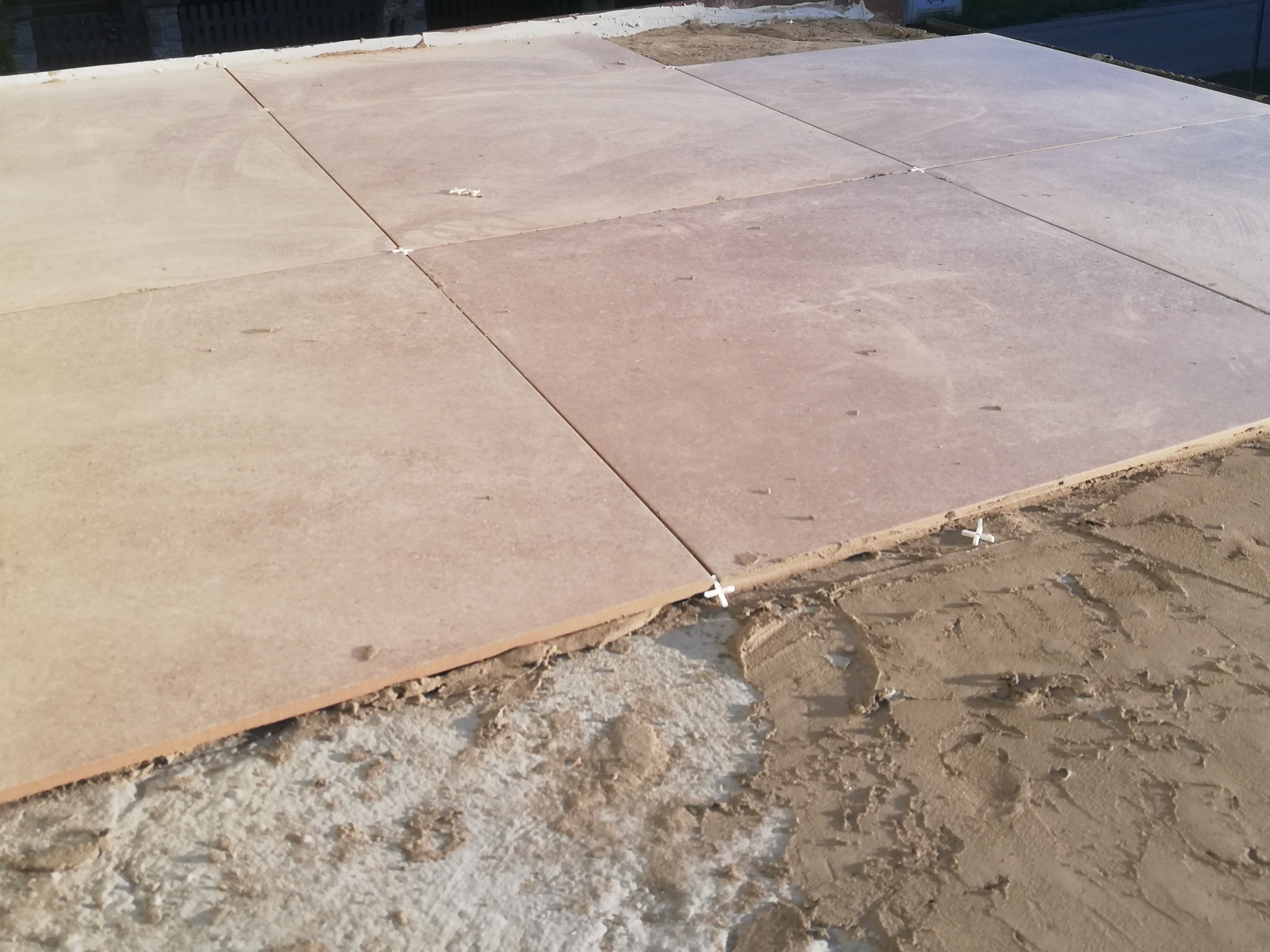 Układanie beżowych płytek podłogowych z użyciem krzyżyków dystansowych na warstwie zaprawy.