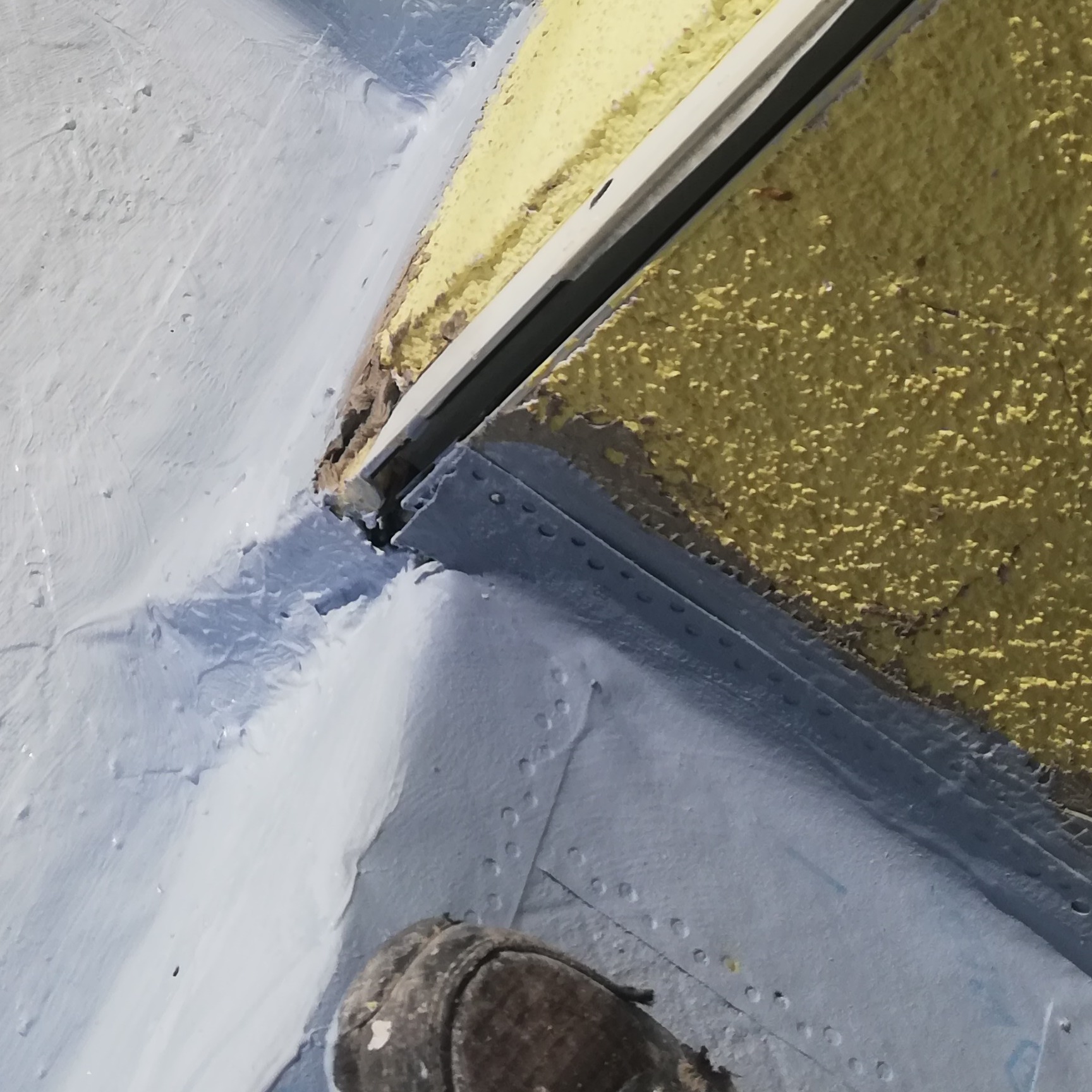 Szpachlowana ściana w narożniku, z widocznym fragmentem buta pracownika, z bliska, świeżo po nałożeniu warstwy szpachli.