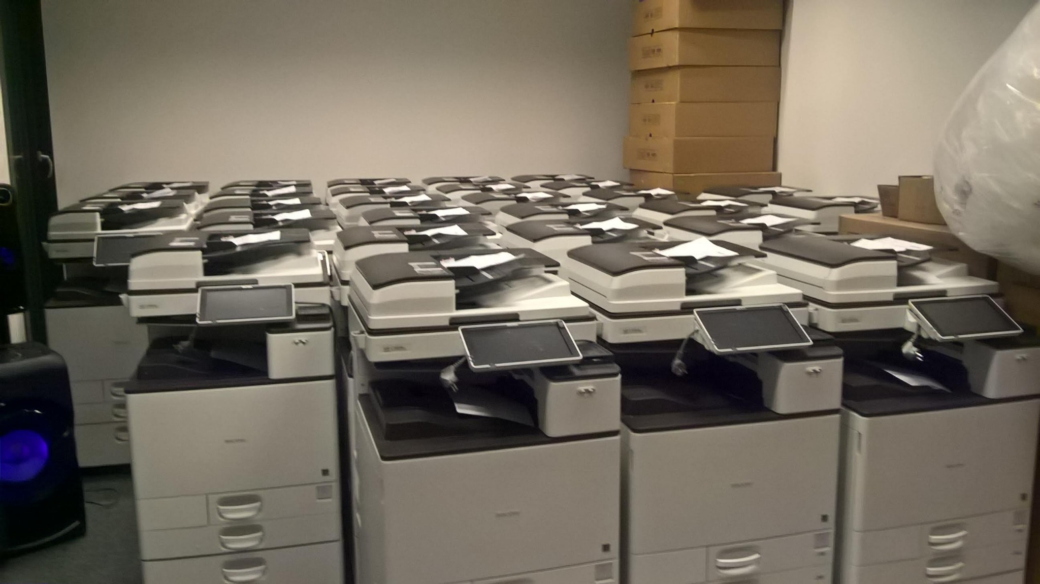 Skladowisko nowych drukarek biurowych w Piasecznie, gotowych do instalacji i konfiguracji, z widocznymi kartonami w tle.