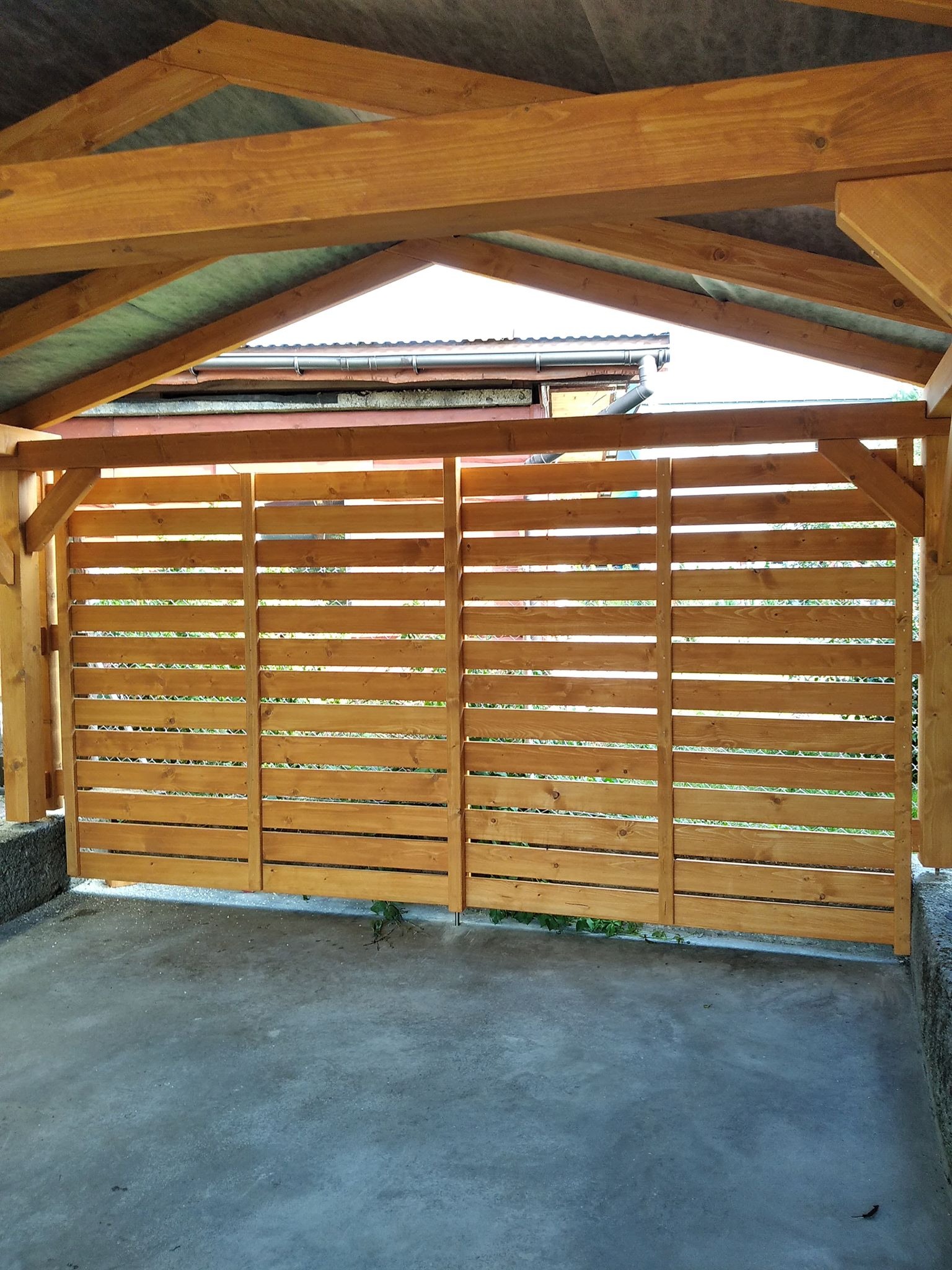 Drewniana konstrukcja z poziomych desek, tworząca ażurową ścianę w Kamienicy, widoczna spod zadaszenia.