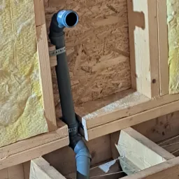 Fragment instalacji kanalizacyjnej z rurą PCV w konstrukcji drewnianej, widoczna izolacja z wełny mineralnej i płyta OSB.