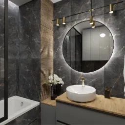 Elegancka łazienka z czarnymi marmurowymi płytkami, okrągłym lustrem z podświetleniem LED, drewnianymi akcentami i złotą armaturą, uzupełniona białymi orchideami w wazonie.