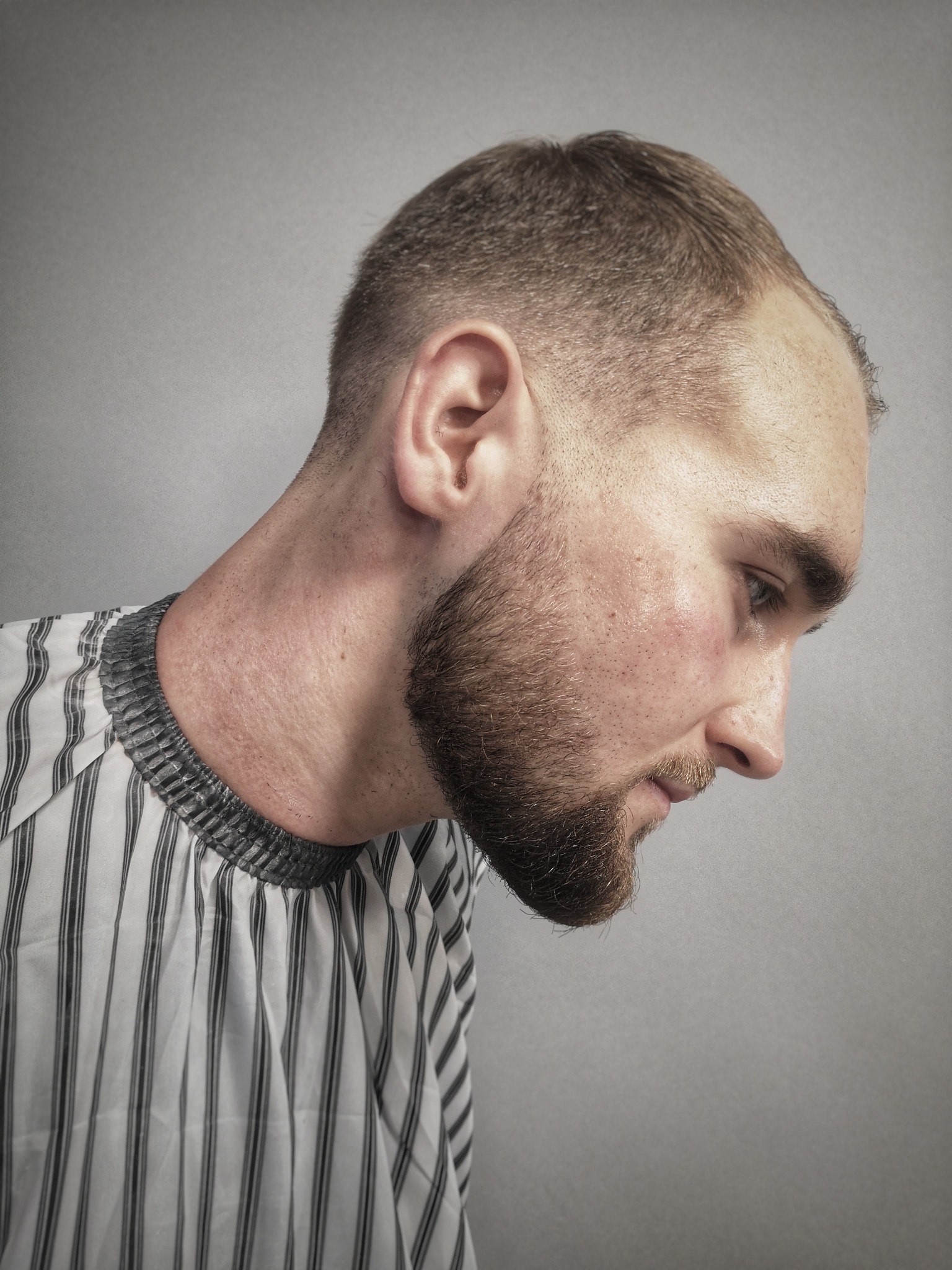 Mężczyzna z krótką fryzurą i brodą, ubrany w pelerynę fryzjerską w paski, profil z bliska, Warszawa.