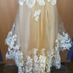 Beżowa suknia ślubna z białymi, koronkowymi aplikacjami kwiatowymi, widoczne detale wykończenia dołu sukni.