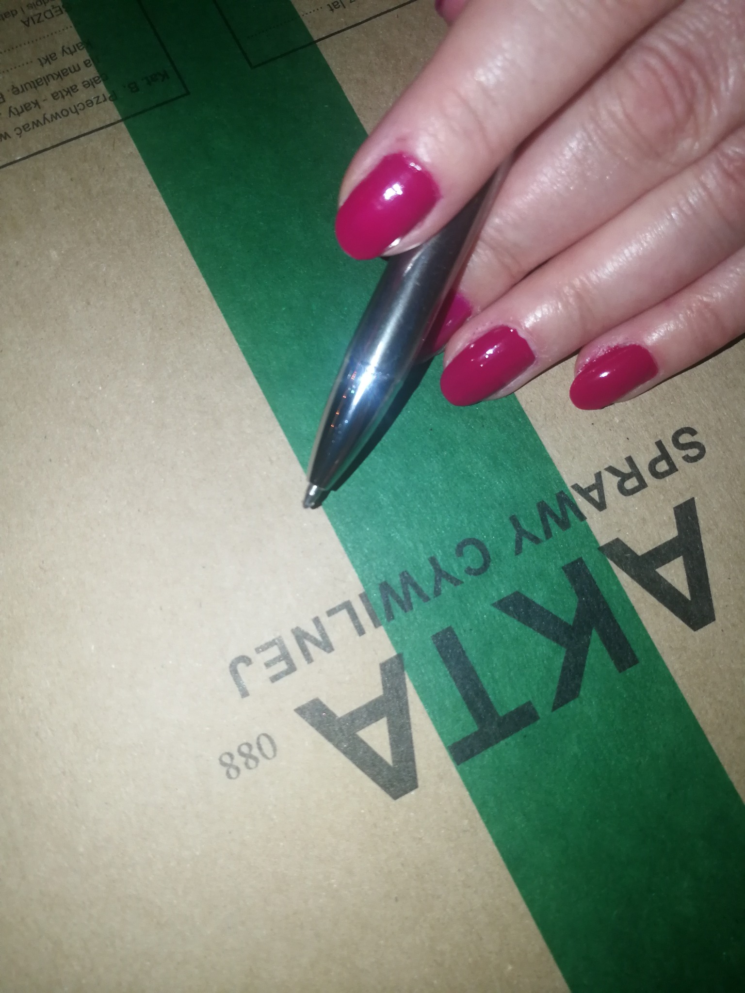 Dłoń z czerwonymi paznokciami trzyma srebrny długopis nad teczką z napisem 'AKTA SPRAWY CYWILNEJ'