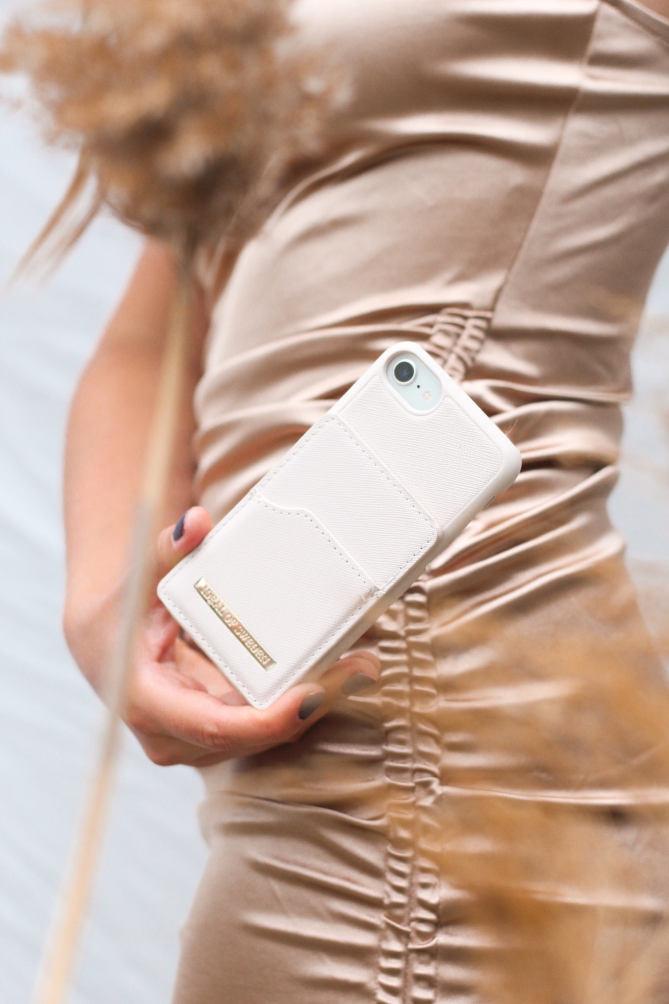 Kobieta w złotej sukience prezentuje białe etui na telefon z kieszonkami na karty i złotym logo marki.
