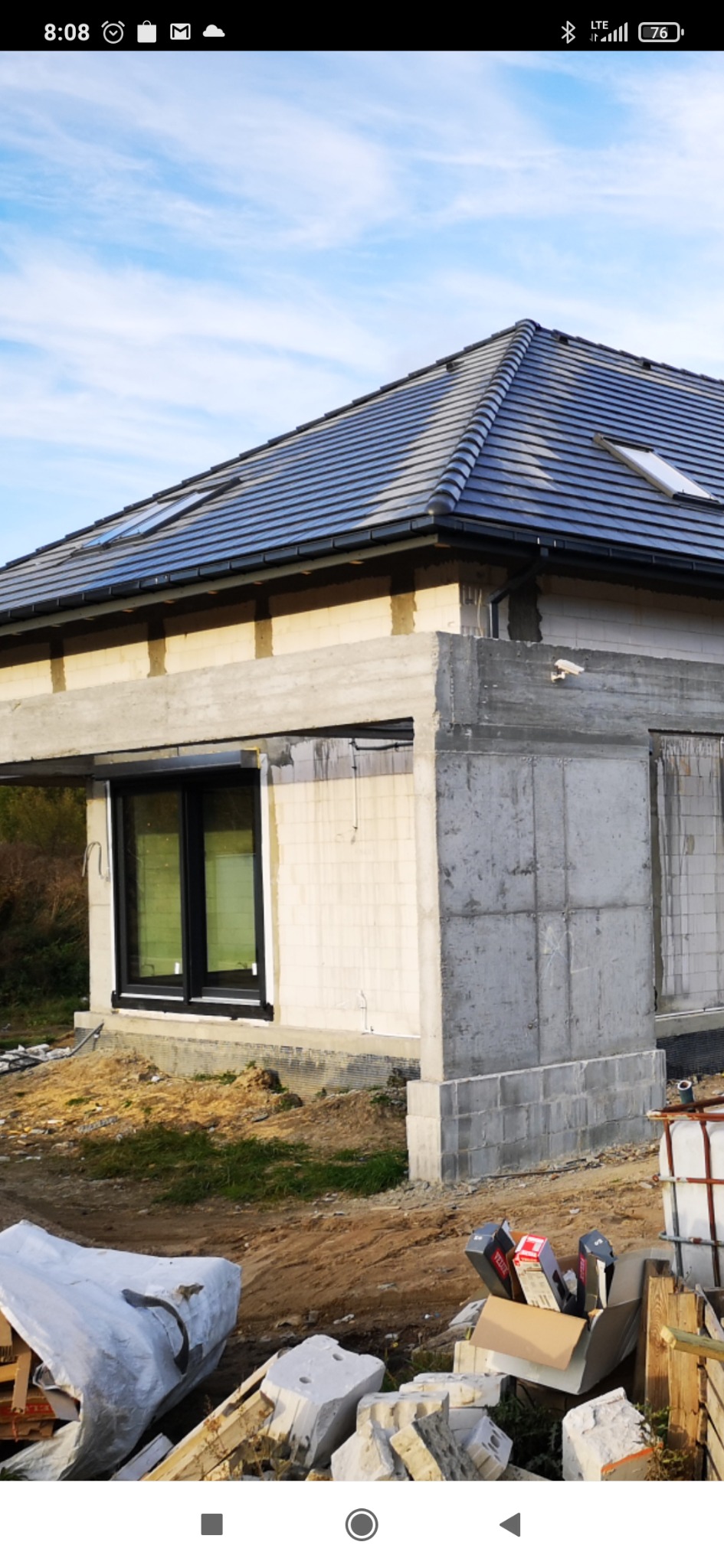 Surowy stan budynku jednorodzinnego w trakcie budowy z widoczną elewacją z betonu komórkowego, oknami z czarną stolarką i dachem z ciemnej dachówki ceramicznej z oknami dachowymi, na pierwszym...