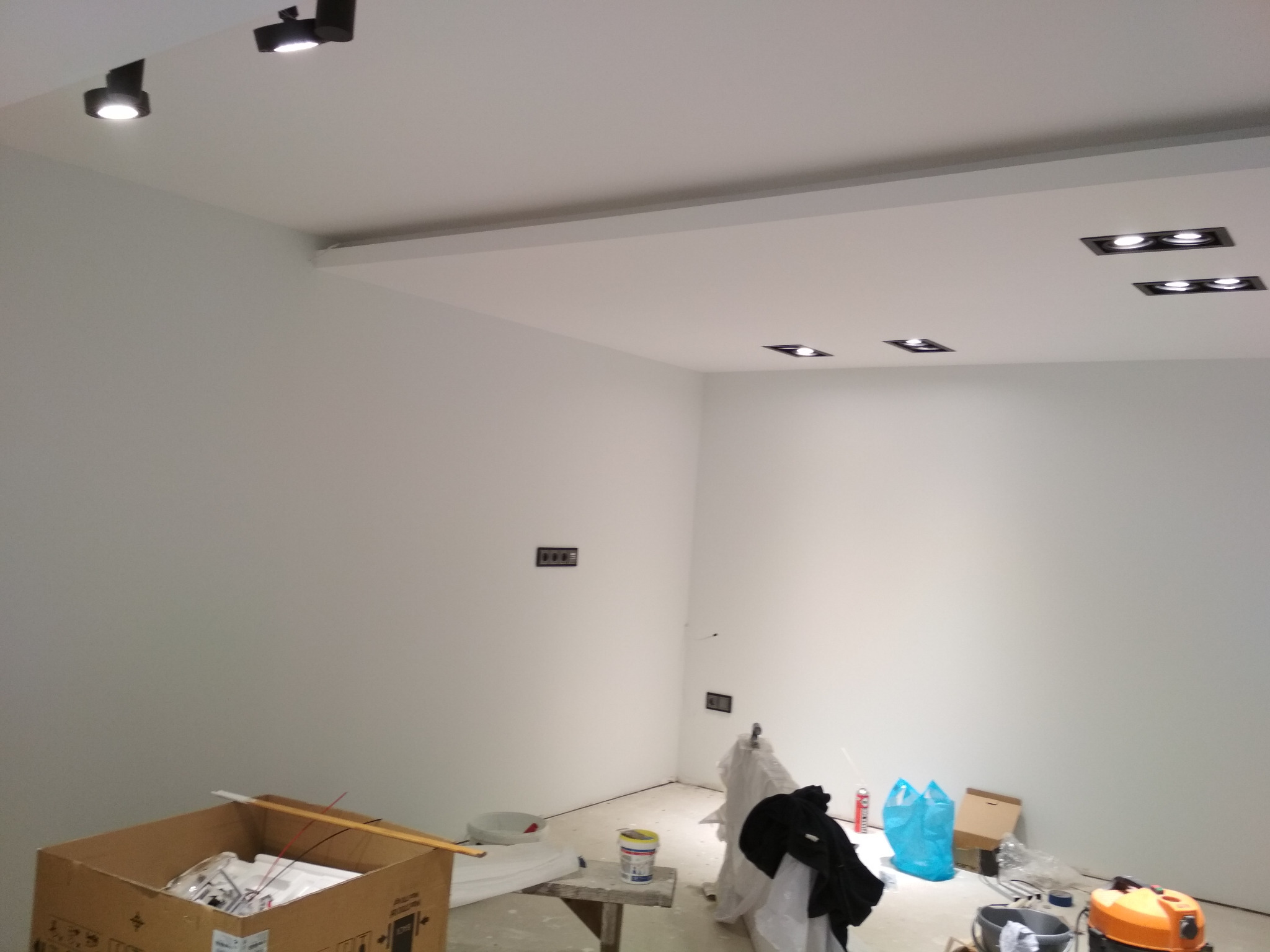 Nowoczesne oświetlenie sufitowe z reflektorami punktowymi i panelami LED w trakcie montażu, widoczne narzędzia i materiały budowlane w pomieszczeniu w stanie surowym.