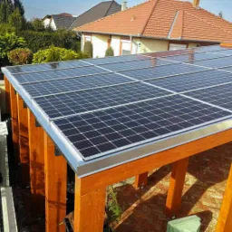 Drewniana konstrukcja z panelami słonecznymi na dachu, widok z zewnątrz, w tle domy jednorodzinne.