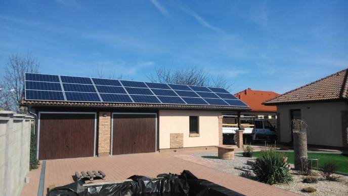 Panele słoneczne na dachu garażu z dwoma bramami, widok z poziomu gruntu, błękitne niebo w tle.