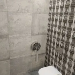 Szara łazienka z płytkami imitującymi beton i dekoracyjną ścianą z motywem okien, wisząca toaleta z chromowanym przyciskiem spłukującym.