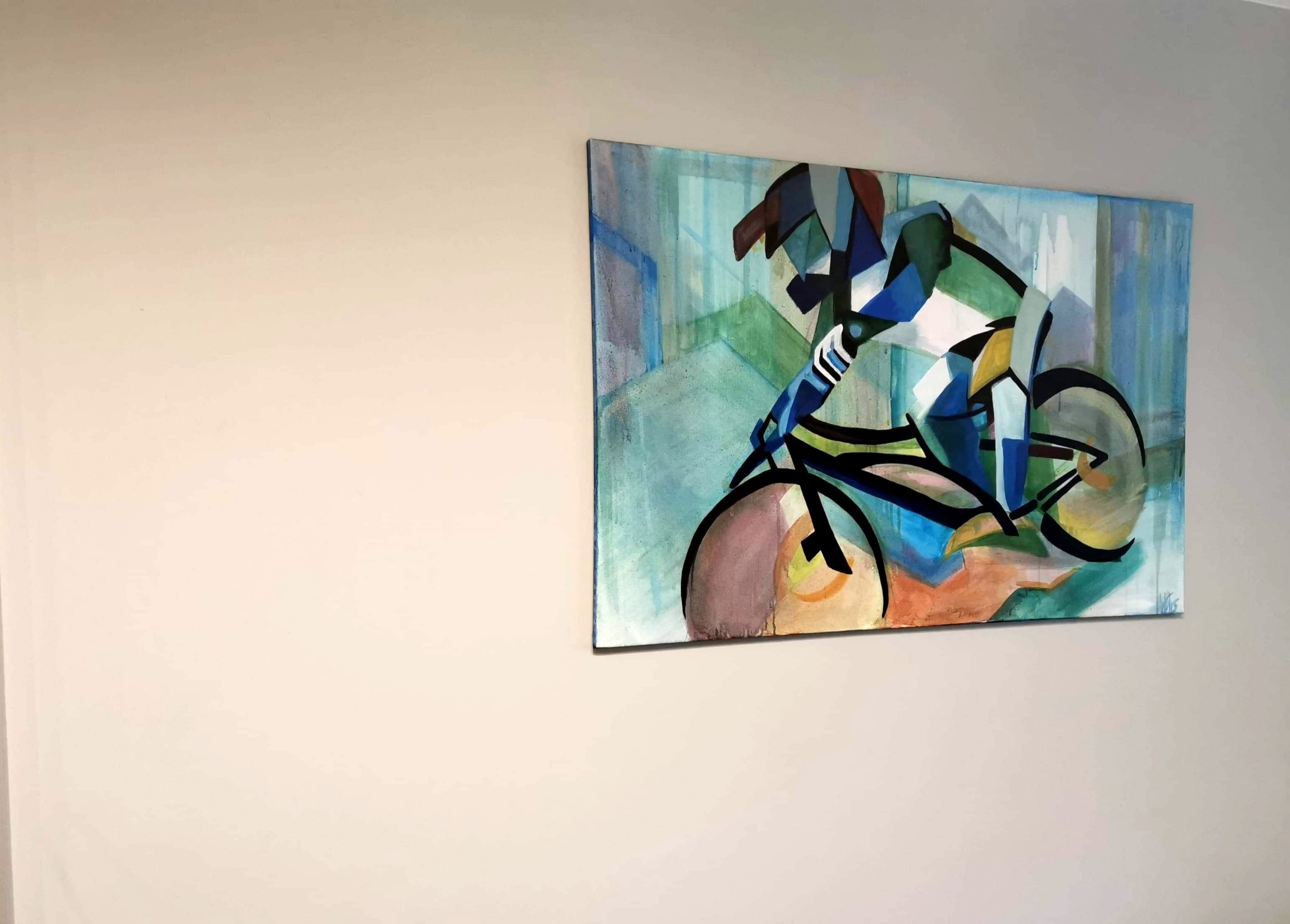 Abstrakcyjny obraz akrylowy na płótnie o wymiarach 115x75cm, przedstawiający kolarza w dynamicznej pozie, utrzymany w tonacji błękitu, zieleni i brązu, zawieszony na jasnej ścianie.