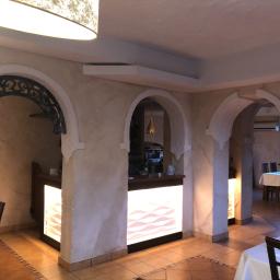 Uslugi Budowlane Piotr Towsciuk - Wnętrze restauracji z łukowymi przejściami wykończonymi szpachlą imitującą kamień, podświetlane bary, i terakotową podłogą.