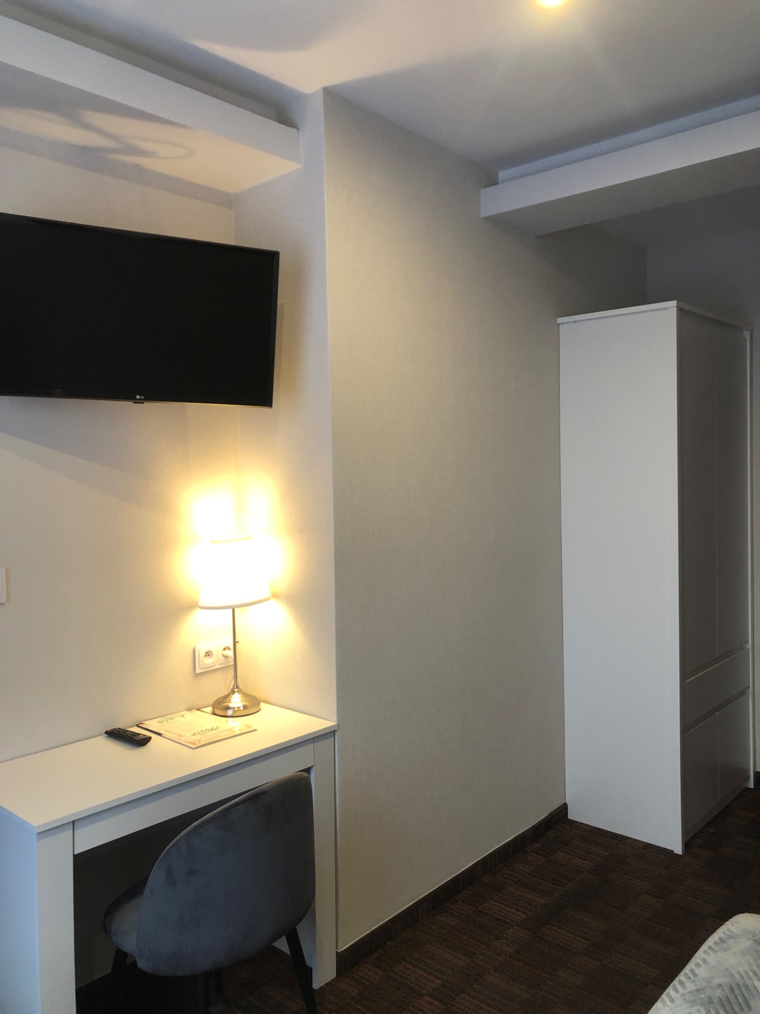 Pokój hotelowy po remoncie: świeżo pomalowane ściany w neutralnym odcieniu, białe meble, ciemna podłoga i oświetlenie tworzą przytulną atmosferę.