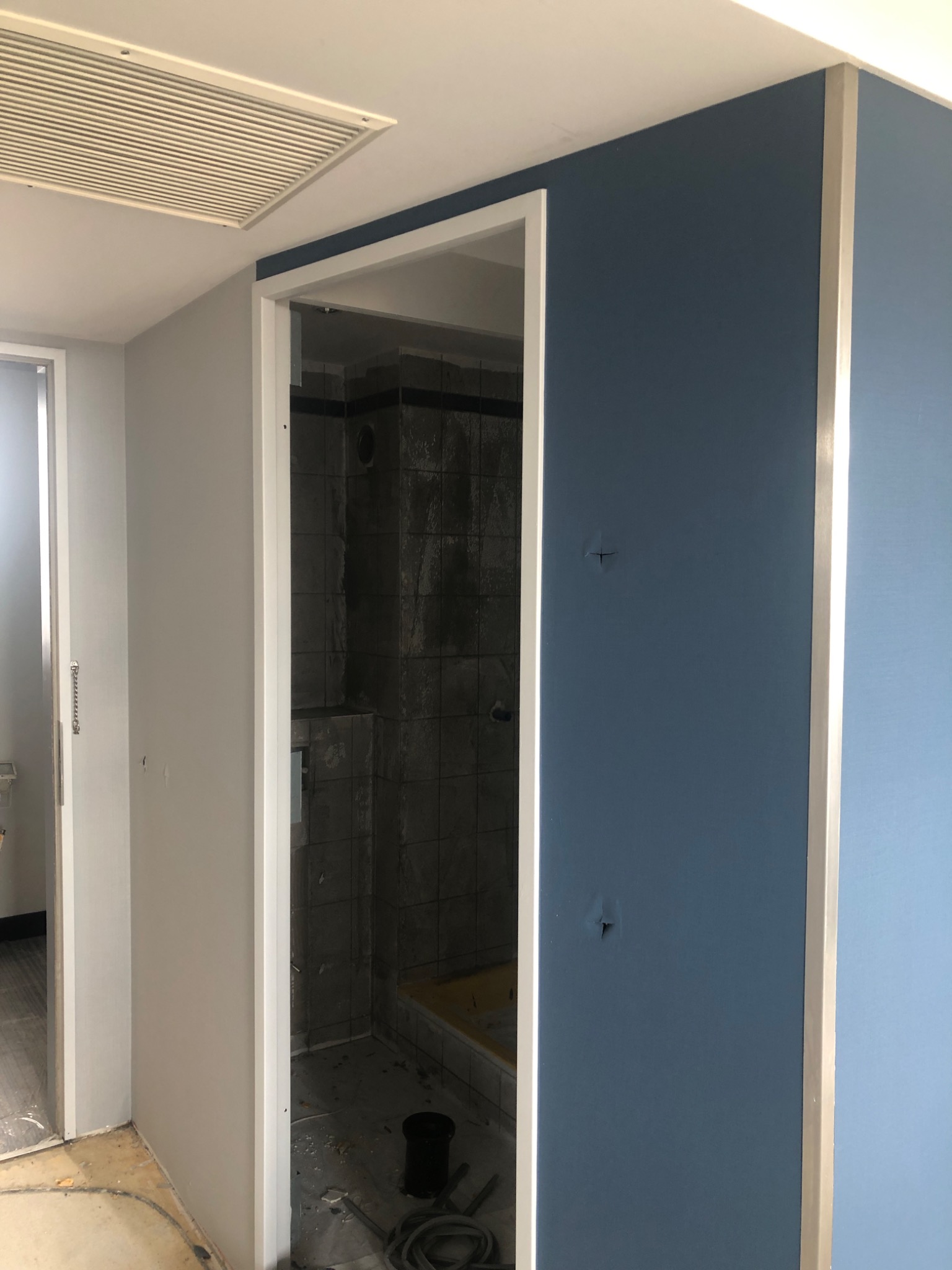 Świeżo pomalowane ściany w odcieniach błękitu i szarości, widoczne niedoskonałości w postaci małych dziur na błękitnej ścianie, fragment łazienki w trakcie remontu z ciemnymi płytkami i żółtą wanną...