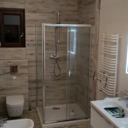 Wykończona łazienka z kabiną prysznicową, toaletą, bidetem, umywalką z szafką i grzejnikiem drabinkowym, wykończona płytkami imitującymi drewno i wzorzystą terakotą.