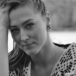 Martyna Święcicka Fotografia - Portret kobiety w czarno-białej tonacji, z ręką opartą o głowę, noszącej kolczyk w nosie i geometryczne kolczyki, na rozmytym tle.