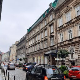 Gabinety Psychoterapii ARIADNA Bielsko-Biała - Ulica w europejskim mieście z kamienicami, samochodami i pieszymi w pochmurny dzień. Widoczny szyld 'Alba Kosmetyczny'