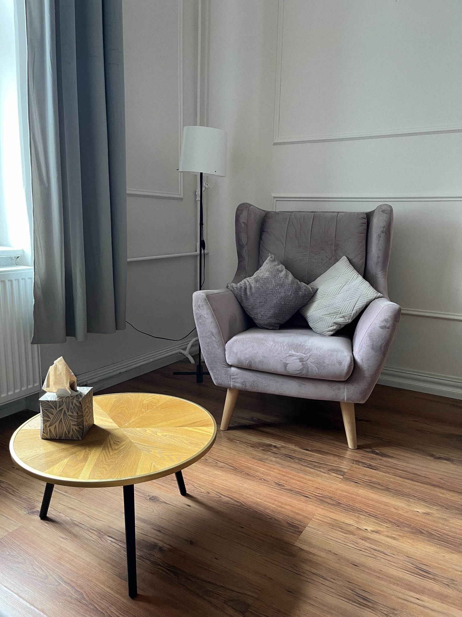 Pokój z fotelem w odcieniach fioletu i stolikiem kawowym z pudełkiem chusteczek, sugerujący przytulne wnętrze gabinetu.