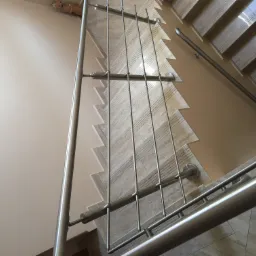 Klatka schodowa z marmurowymi schodami i nowoczesną, metalową balustradą z pionowymi prętami oraz poręczą, widok z góry.