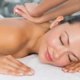 Kobieta z zamkniętymi oczami relaksuje się podczas masażu pleców na białym ręczniku w gabinecie.