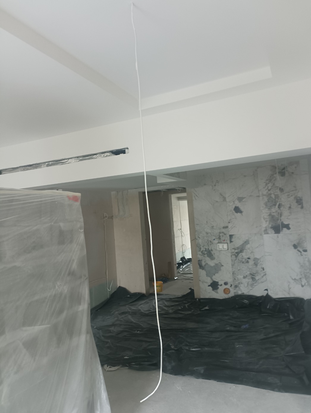 Wnętrze w trakcie prac wykończeniowych: zabezpieczona folią ściana, podłoga przykryta czarną folią ochronną, widoczne kable i surowa ściana z imitacją marmuru w tle.