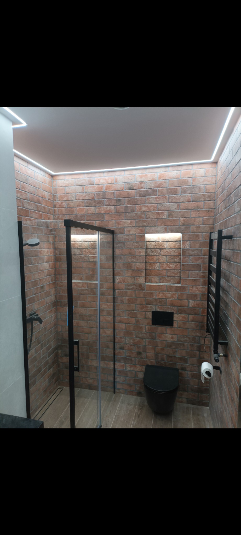 Nowoczesna łazienka z kabiną prysznicową typu walk-in, wykończona cegłą i oświetleniem LED podsufitowym.