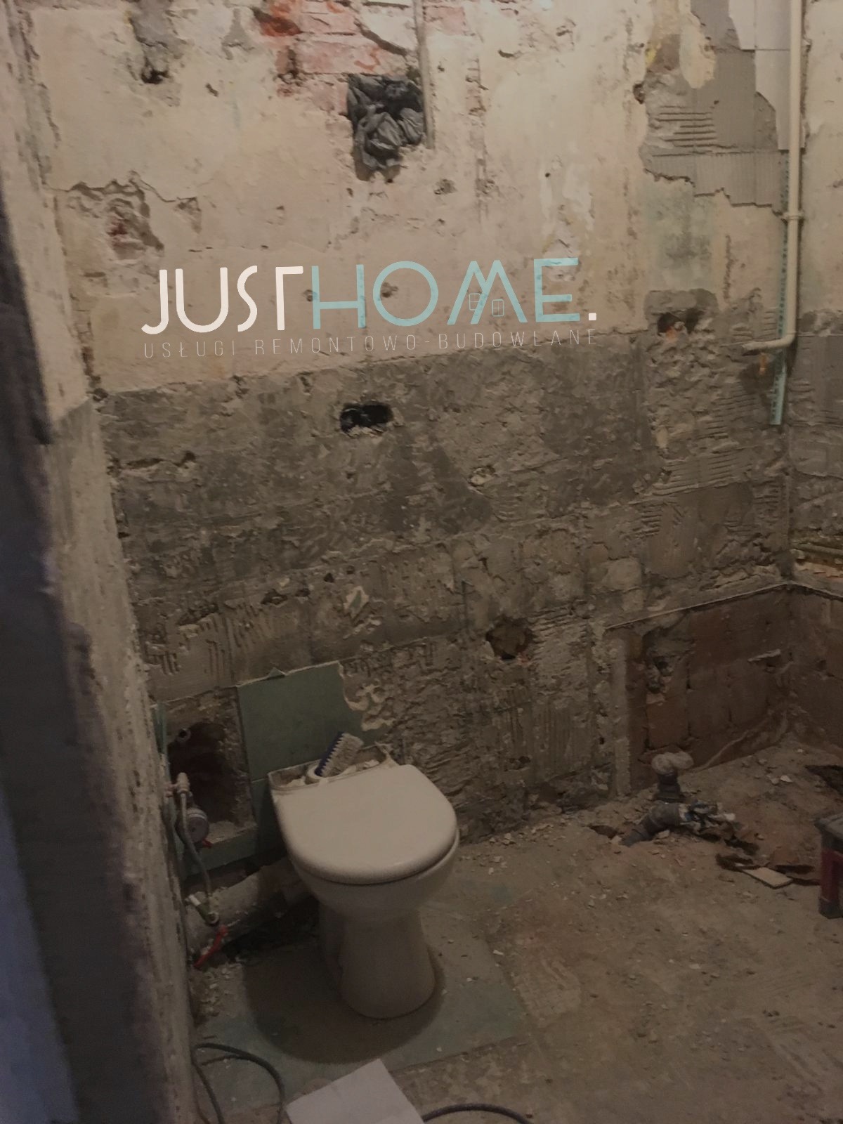 Łazienka w trakcie demontażu starych płytek, widoczne odsłonięte fragmenty cegieł i resztki kleju, toaleta pozostała na miejscu, logo firmy na ścianie.
