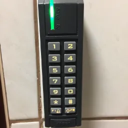 Czarny panel numeryczny Roger z zieloną diodą LED, zamontowany na kafelkach ściennych, widoczne przyciski z cyframi i symbolami.