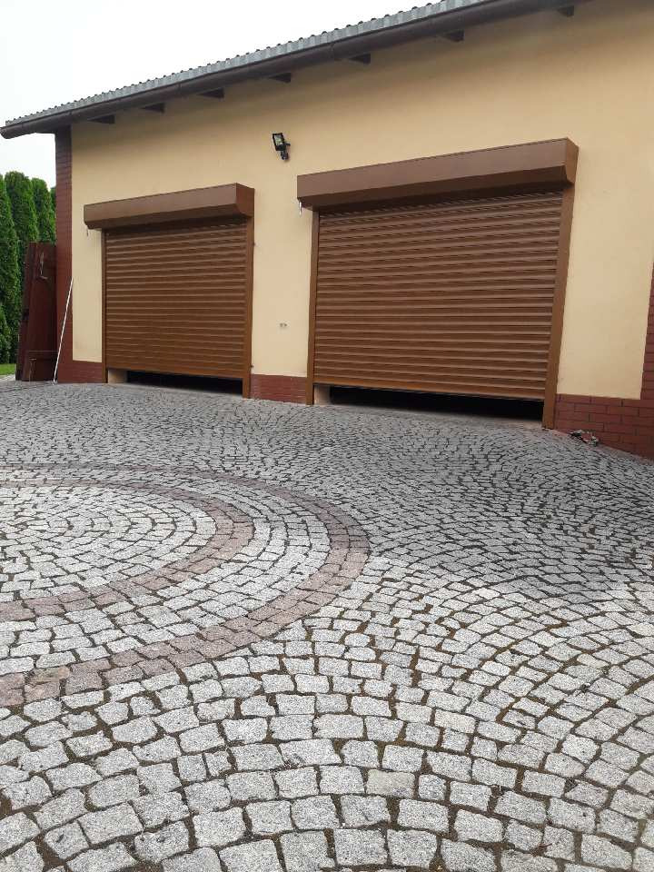 Dwa brązowe zamknięte systemy osłonowe na garażu z beżową elewacją i dekoracyjną kostką brukową na podjeździe.